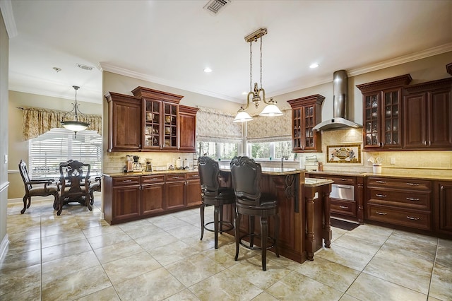 kitchen featuring wall chimney range hood, hanging light fixtures, backsplash, and light tile floors