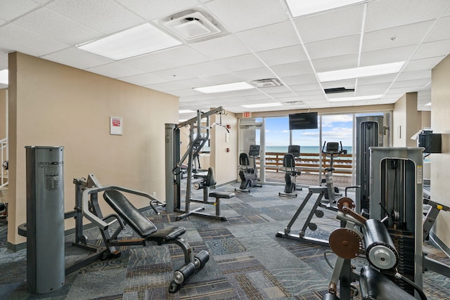 gym with carpet floors, a wall of windows, and a drop ceiling