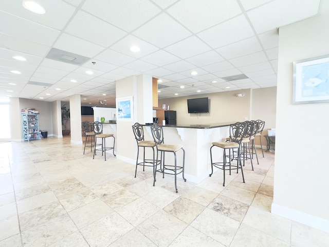 kitchen with kitchen peninsula, a breakfast bar, and a drop ceiling