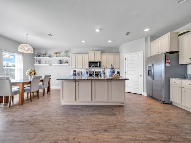 kitchen with wood-type flooring, decorative light fixtures, a center island with sink, and stainless steel appliances