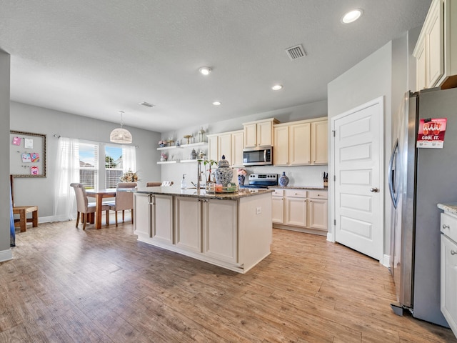 kitchen with stainless steel appliances, light hardwood / wood-style floors, a kitchen island with sink, and decorative light fixtures