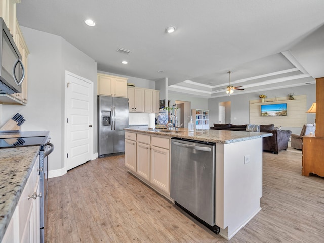 kitchen with sink, a center island with sink, light hardwood / wood-style flooring, a tray ceiling, and stainless steel appliances