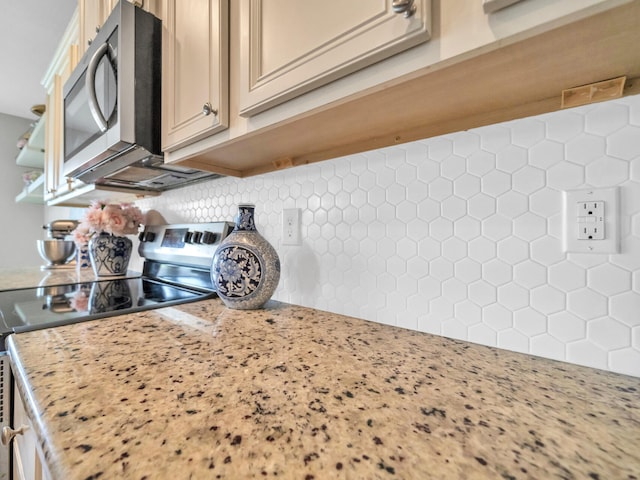 kitchen with light stone countertops, stainless steel appliances, cream cabinets, and tasteful backsplash