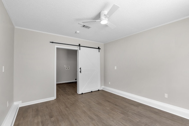 unfurnished bedroom with hardwood / wood-style flooring, ceiling fan, a barn door, ornamental molding, and a textured ceiling