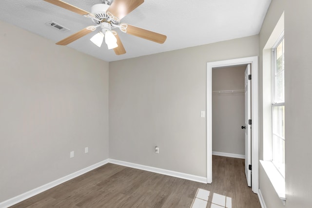 unfurnished bedroom with hardwood / wood-style floors, a walk in closet, a closet, and ceiling fan