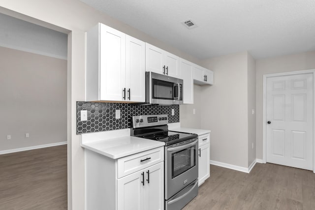 kitchen with hardwood / wood-style floors, backsplash, a textured ceiling, appliances with stainless steel finishes, and white cabinetry