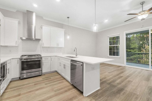 kitchen featuring wall chimney range hood, appliances with stainless steel finishes, white cabinets, decorative light fixtures, and kitchen peninsula