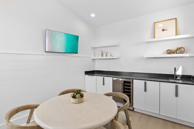 dining area featuring indoor wet bar, vaulted ceiling, beverage cooler, and light hardwood / wood-style flooring