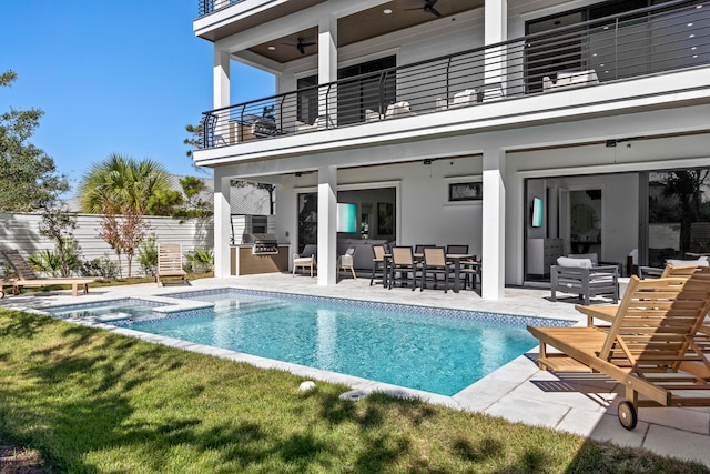 rear view of property featuring a patio, a balcony, an outdoor kitchen, and a pool with hot tub