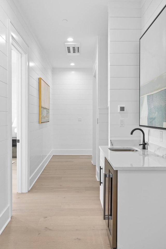 hall with sink, beverage cooler, and light wood-type flooring