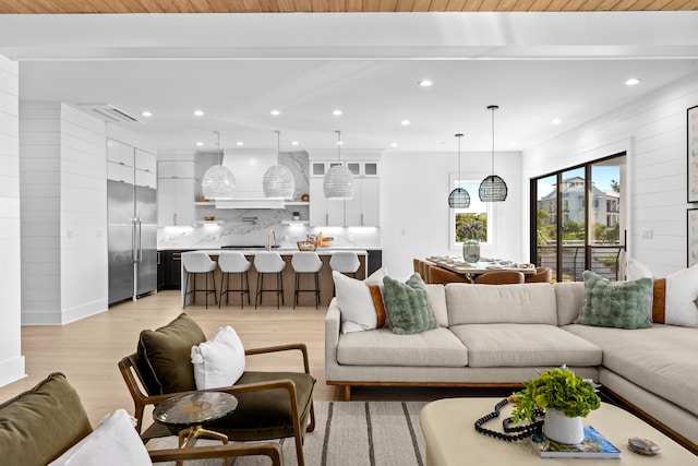 living room with beamed ceiling, light wood-type flooring, and sink