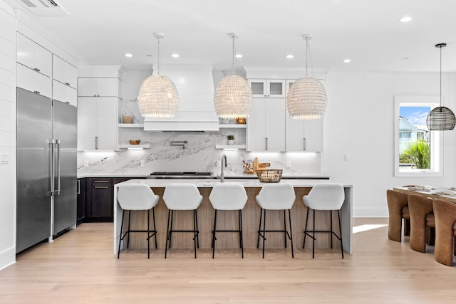 kitchen with pendant lighting, stainless steel built in refrigerator, a kitchen island with sink, and tasteful backsplash