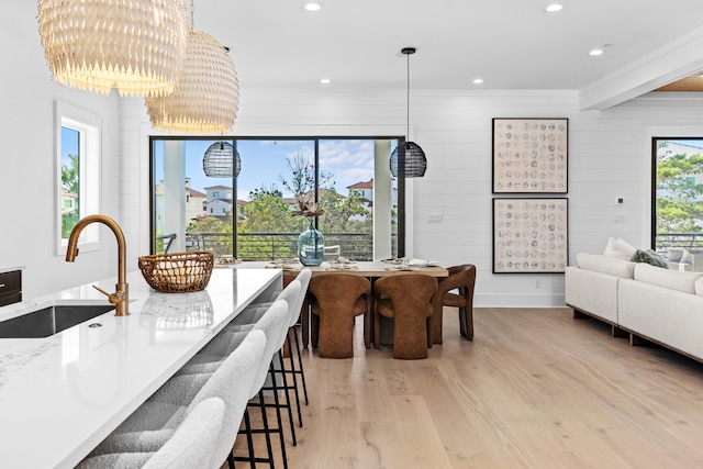 dining area featuring a notable chandelier, wood walls, sink, and light hardwood / wood-style flooring