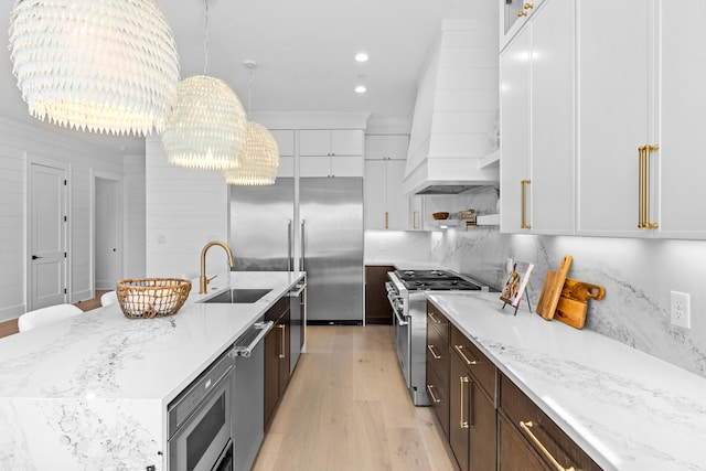 kitchen with built in appliances, white cabinets, pendant lighting, and custom exhaust hood