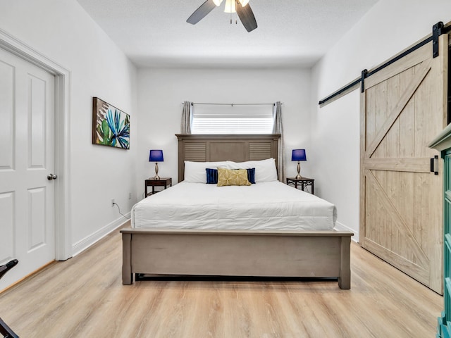 bedroom with ceiling fan, a barn door, a textured ceiling, and light wood-type flooring