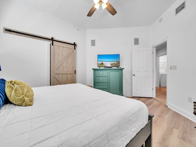 bedroom featuring ceiling fan, a barn door, and light hardwood / wood-style flooring