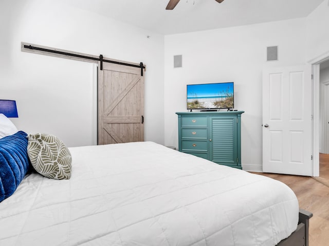 bedroom with hardwood / wood-style flooring, a barn door, and ceiling fan