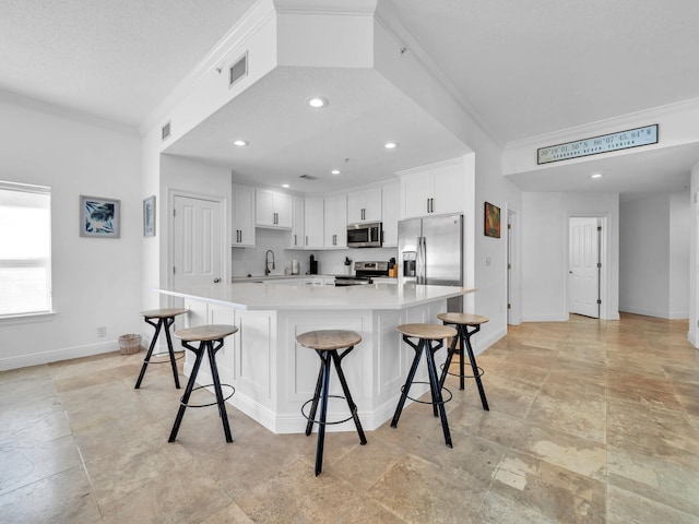 kitchen featuring a large island, a breakfast bar, stainless steel appliances, ornamental molding, and white cabinets