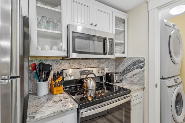 kitchen featuring light stone countertops, stacked washer / dryer, white cabinets, stainless steel appliances, and decorative backsplash