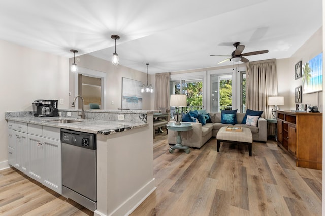 kitchen featuring stainless steel dishwasher, light stone counters, sink, decorative light fixtures, and white cabinetry