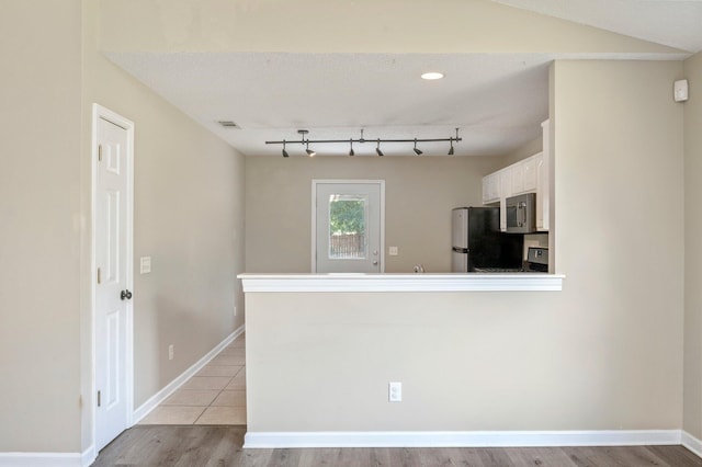 kitchen featuring light wood-type flooring, white cabinetry, kitchen peninsula, and fridge