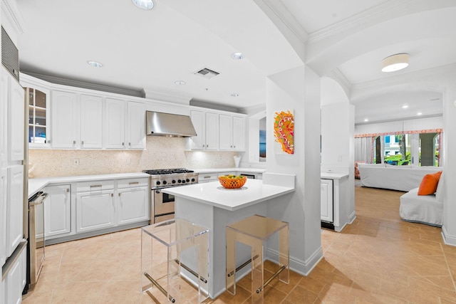 kitchen with white cabinetry, wall chimney range hood, a kitchen bar, high end stainless steel range, and ornamental molding