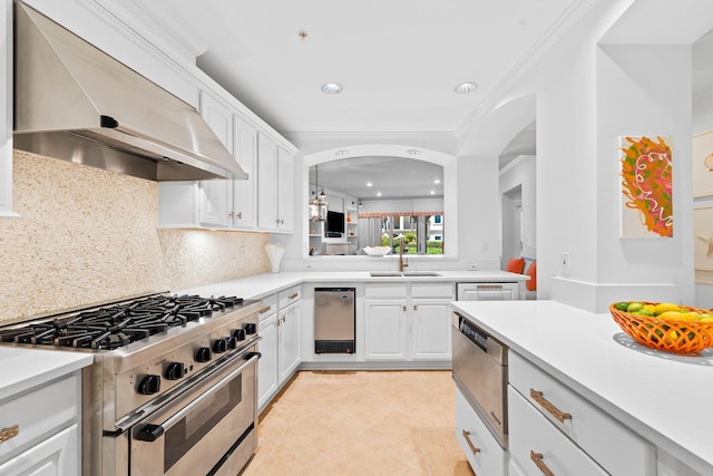 kitchen with tasteful backsplash, high end stove, sink, wall chimney range hood, and white cabinetry