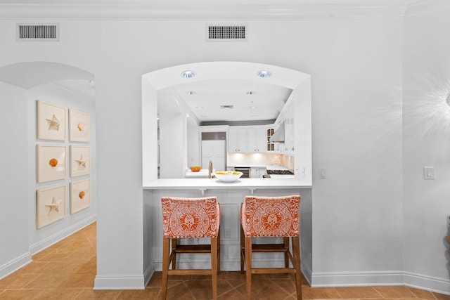 kitchen with white cabinetry, sink, crown molding, extractor fan, and a kitchen bar