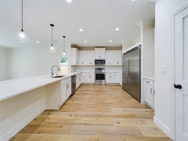 kitchen with hanging light fixtures, sink, white cabinetry, appliances with stainless steel finishes, and light hardwood / wood-style floors