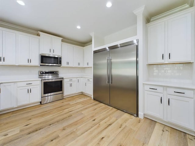 kitchen with appliances with stainless steel finishes, light wood-type flooring, white cabinetry, and ornamental molding