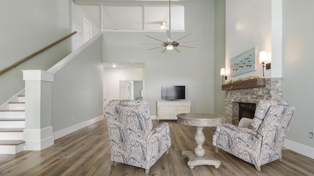 living room featuring a ceiling fan, stairway, wood finished floors, and a stone fireplace