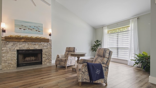 sitting room with vaulted ceiling, a stone fireplace, ceiling fan, and hardwood / wood-style flooring