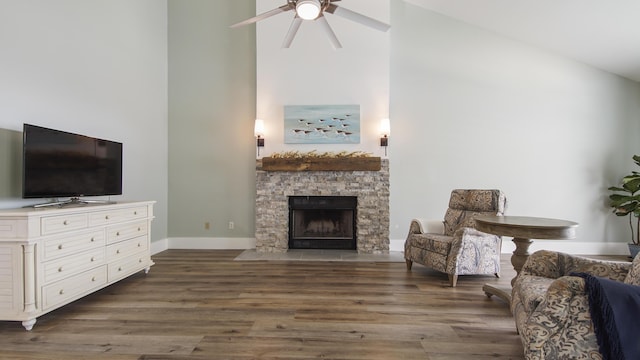 sitting room with dark wood-style floors, high vaulted ceiling, a stone fireplace, and baseboards