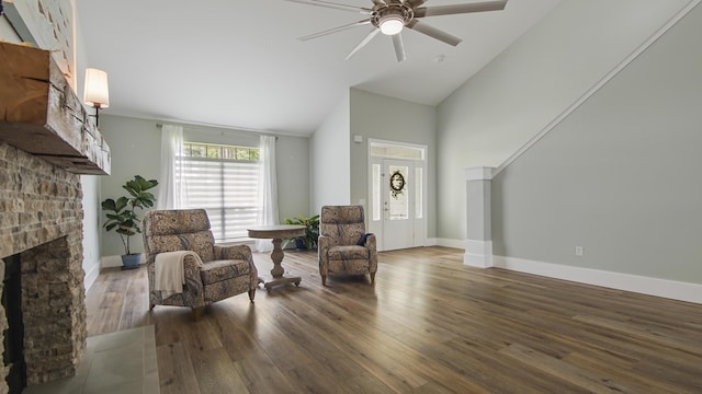 sitting room featuring dark wood-style floors, ceiling fan, a stone fireplace, and baseboards