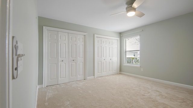 unfurnished bedroom with multiple closets, light carpet, baseboards, and a ceiling fan