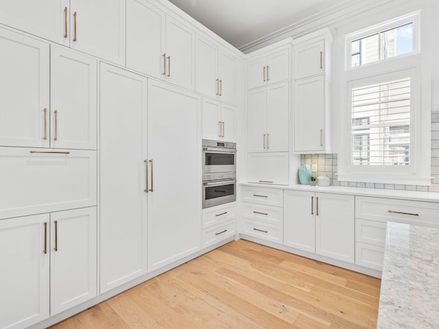 kitchen with tasteful backsplash, light stone counters, light hardwood / wood-style flooring, double oven, and white cabinets