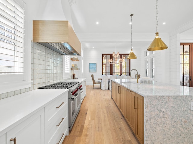 kitchen featuring white cabinetry, light stone countertops, hanging light fixtures, an island with sink, and range with two ovens