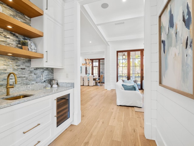 bar with light stone countertops, white cabinetry, sink, beverage cooler, and light wood-type flooring