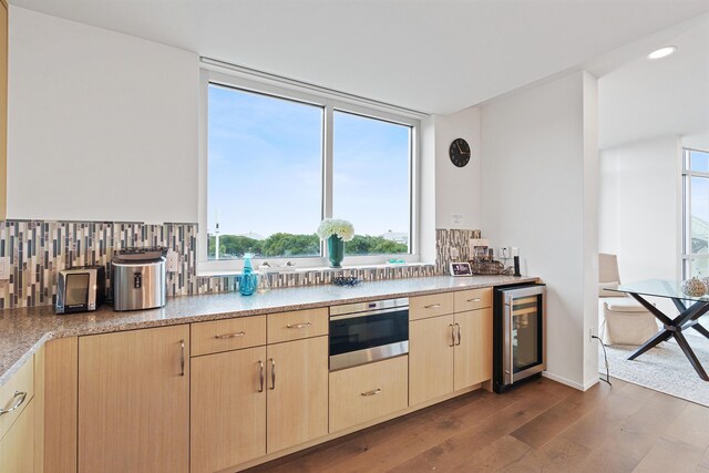 kitchen with stainless steel oven, wood-type flooring, light brown cabinetry, decorative backsplash, and wine cooler