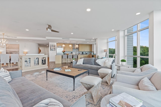 living room with ceiling fan with notable chandelier, light hardwood / wood-style floors, and a wall of windows