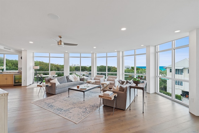 living room featuring expansive windows, ceiling fan, a water view, light wood-type flooring, and wine cooler