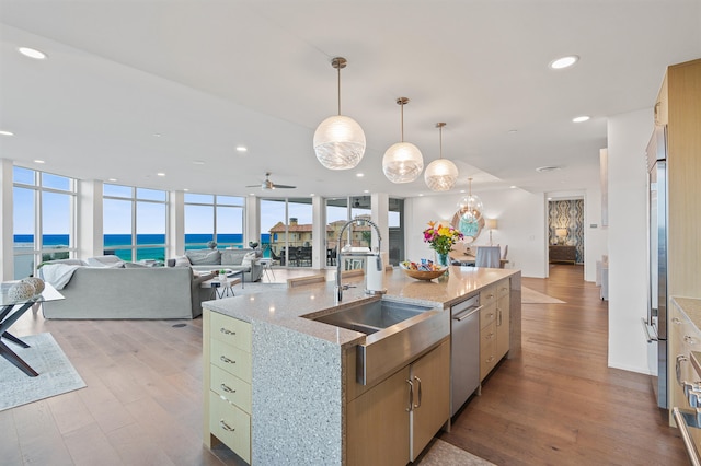 kitchen with light hardwood / wood-style flooring, a center island with sink, sink, light stone counters, and a water view