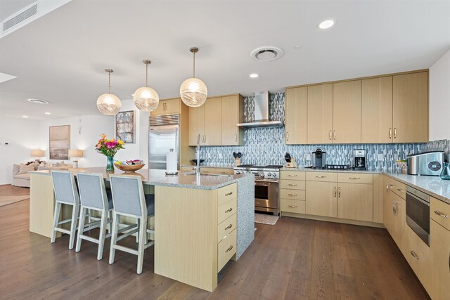 kitchen featuring built in appliances, wall chimney range hood, backsplash, a kitchen island with sink, and dark hardwood / wood-style flooring