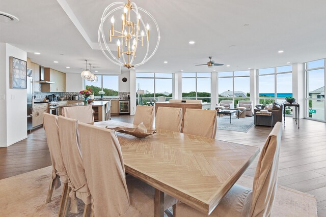 dining area featuring a wall of windows, light hardwood / wood-style flooring, a healthy amount of sunlight, and ceiling fan with notable chandelier