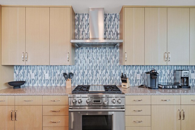 kitchen featuring wall chimney range hood, light brown cabinets, backsplash, and stainless steel stove