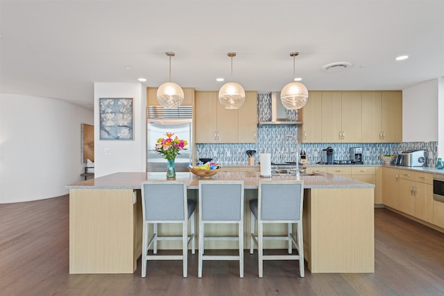 kitchen with built in fridge, hardwood / wood-style flooring, a center island with sink, and tasteful backsplash