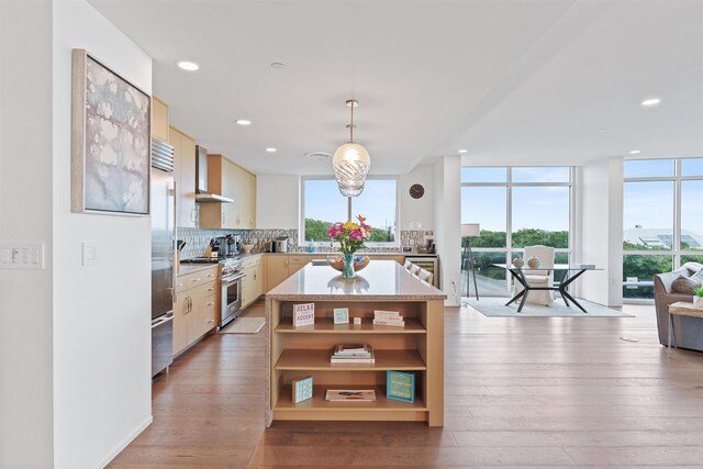 kitchen featuring light hardwood / wood-style flooring, high end appliances, a kitchen island, decorative backsplash, and wall chimney exhaust hood