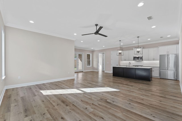 kitchen featuring white cabinets, light wood-type flooring, an island with sink, decorative light fixtures, and stainless steel appliances