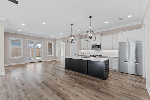 kitchen with sink, hanging light fixtures, stainless steel appliances, a center island with sink, and white cabinets