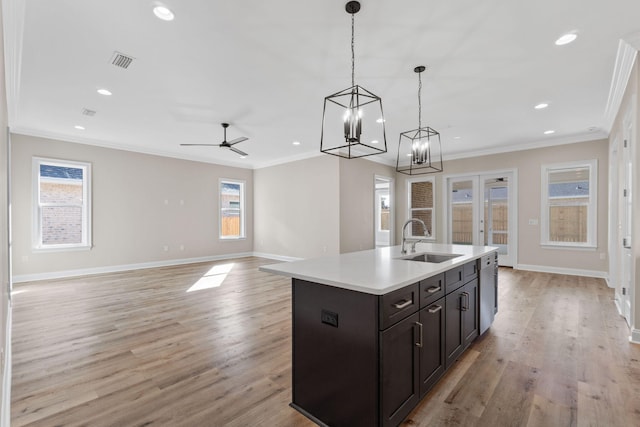 kitchen with light wood-type flooring, ceiling fan with notable chandelier, sink, decorative light fixtures, and an island with sink